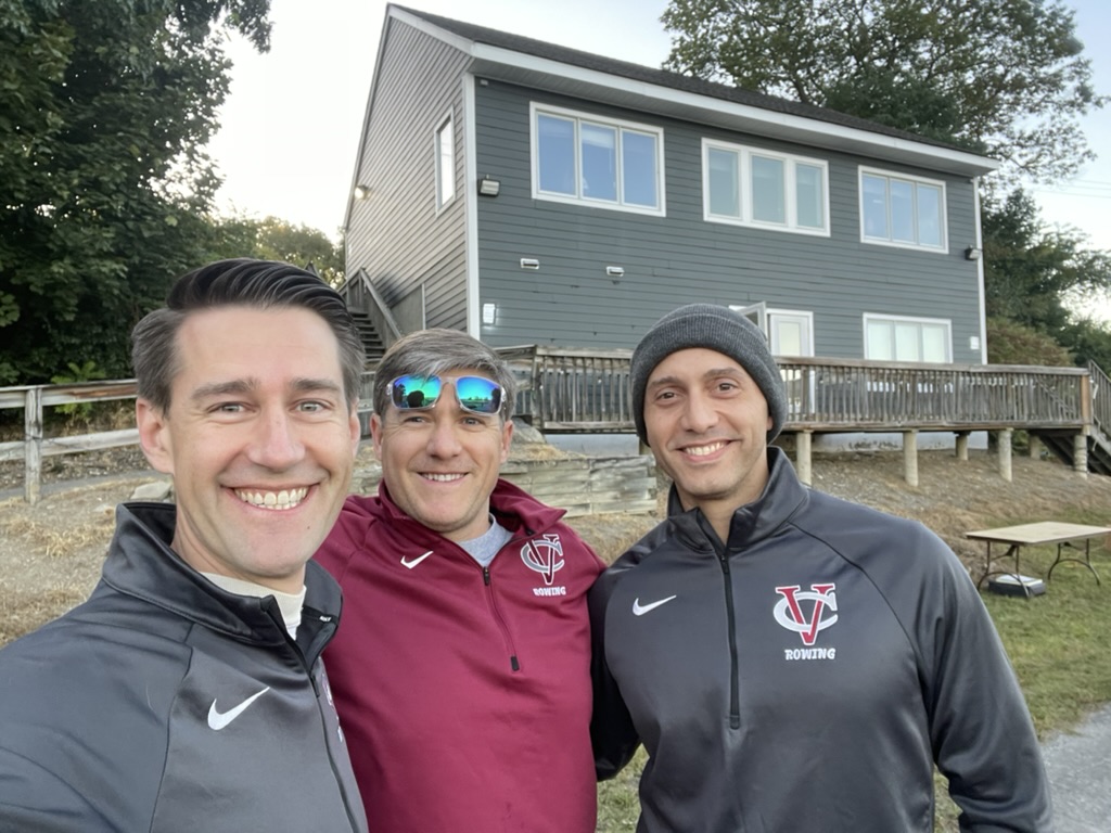 Three alumni in VC Rowing gear in front of the boathouse